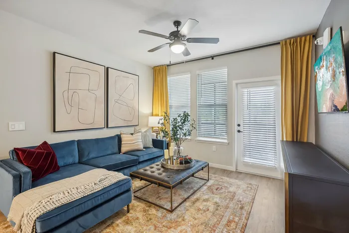 Bright and modern living room featuring a luxurious blue sectional sofa, abstract artwork, and a cozy ambiance with ample natural light.