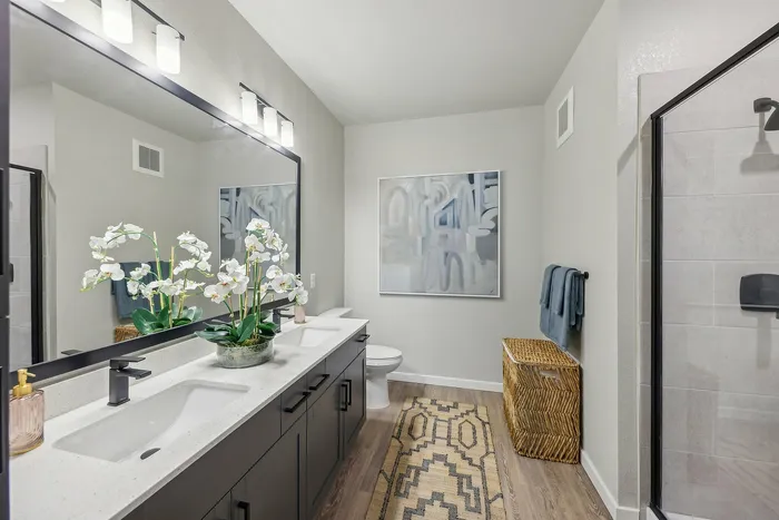 Elegant bathroom featuring a double vanity with sleek fixtures, a stylish shower, and tasteful decor including a large mirror, floral arrangement, and abstract art.