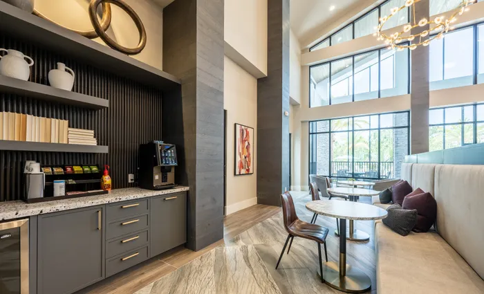 Modern apartment community space with elegant seating, high ceilings, and abundant natural light through large windows.