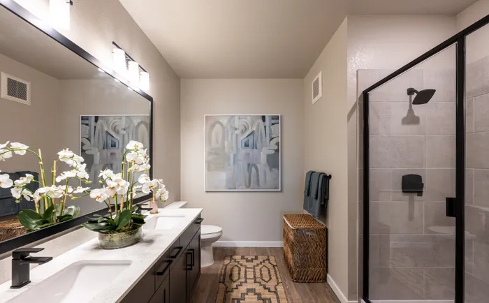 Elegant bathroom with a modern double vanity, large mirror, and a sleek glass shower, accentuated by stylish decor and warm lighting.