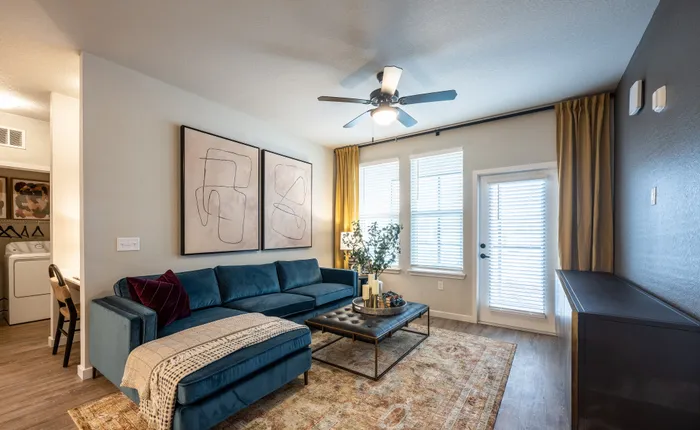 Chic living room with plush teal sectional, abstract wall art, and abundant natural light from large windows.