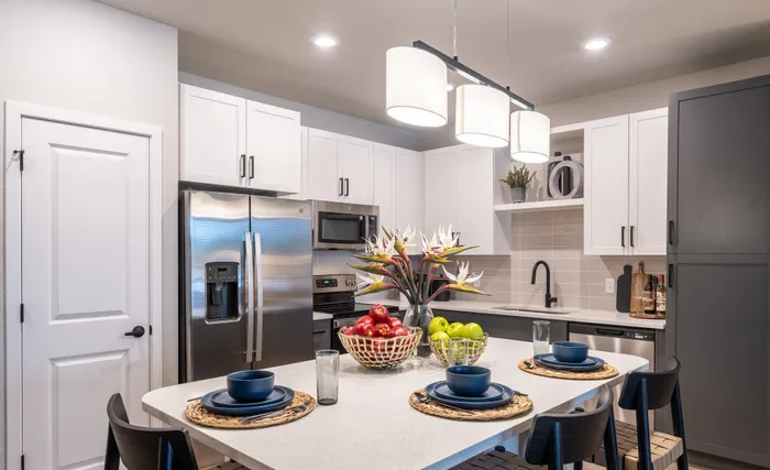Modern kitchen featuring sleek white cabinetry, stainless steel appliances, and elegant pendant lighting, with a stylish breakfast bar set for dining.