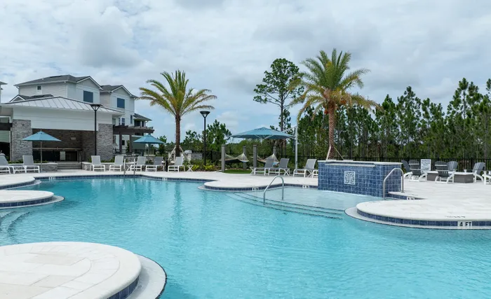Luxurious apartment complex showcasing a stunning outdoor pool area surrounded by palm trees and comfortable lounge chairs, perfect for relaxation.