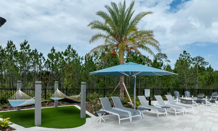 Luxurious apartment complex with a resort-style pool and palm tree-lined surroundings, perfect for relaxation under a clear blue sky.