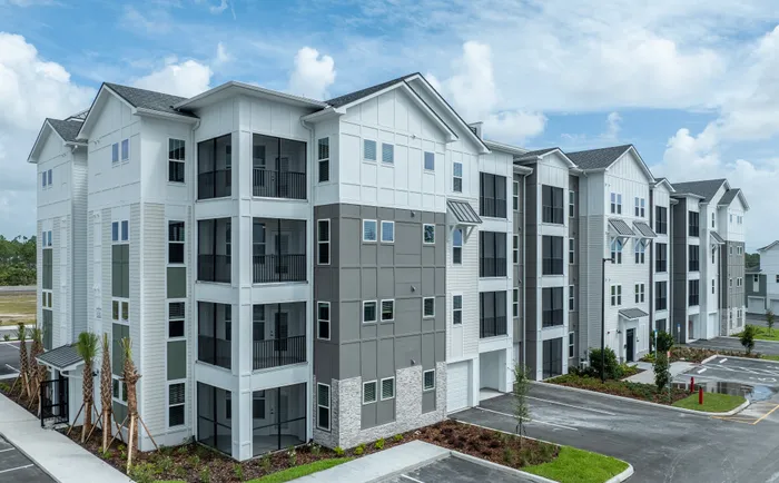 Modern apartment complex with stylish architecture, featuring spacious balconies, sleek design, and lush landscaping under a vibrant blue sky.