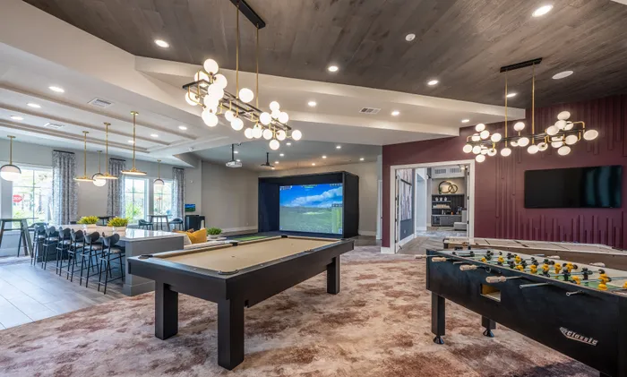 Luxurious recreation room with modern lighting, featuring a pool table, foosball table, and a golf simulator for entertainment.