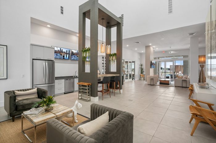 Modern apartment lounge featuring chic seating, elegant pendant lighting, and a sleek kitchen area with stainless steel appliances.