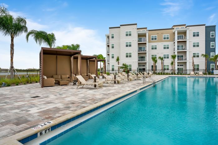 Luxurious apartment complex with a stunning outdoor pool, elegant lounge chairs, and stylish cabanas, surrounded by lush palm trees.