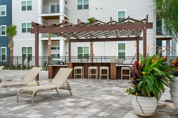 Inviting outdoor area with stylish pergola, modern bar seating, and cozy lounge chairs accented by vibrant potted plants, perfect for relaxation and enjoyment.