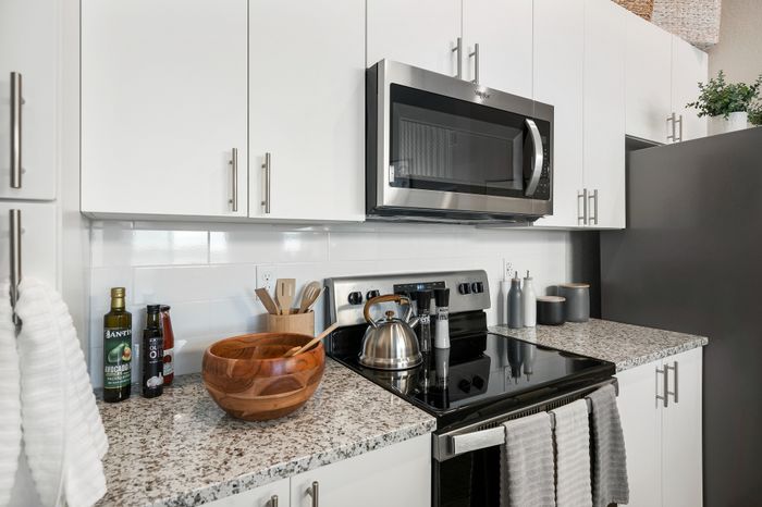 Modern kitchen with sleek white cabinets, stainless steel microwave, and elegant granite countertops.
