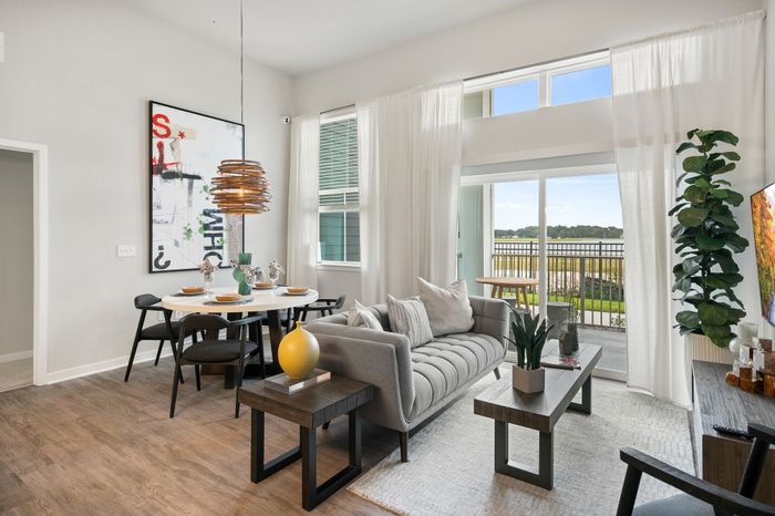 Chic open-plan living room with modern gray sofa, elegant dining set, and floor-to-ceiling windows revealing a serene outdoor view.