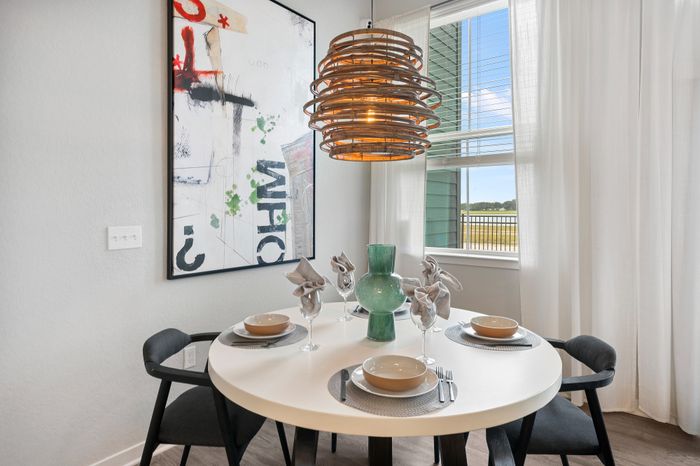Elegant dining area with a modern, round table set for four, featuring stylish black chairs and a unique, artistic light fixture. Large window with sheer curtains offers a bright, inviting atmosphere.