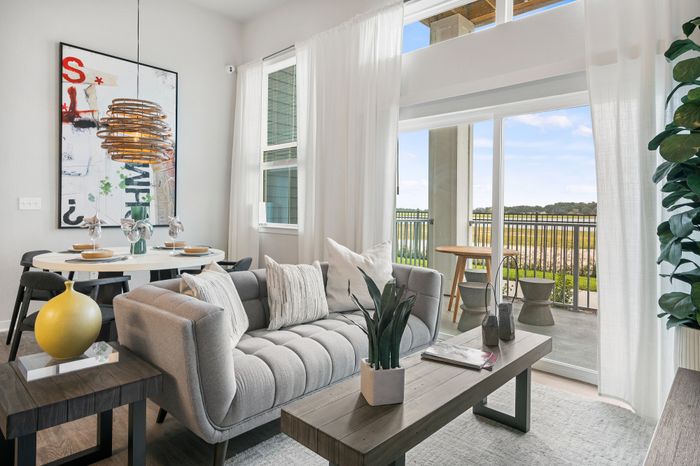 Sunlit modern living room with elegant decor, featuring a cozy grey sofa, stylish dining area, and scenic balcony view.