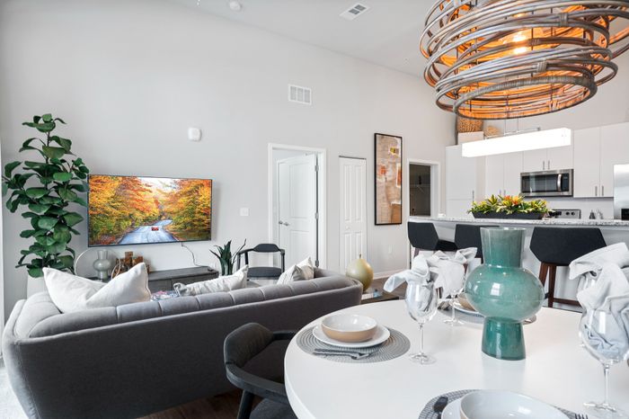 Modern apartment interior with an open-concept living room, stylish kitchen, and elegant dining area. Features include a cozy gray sofa, vibrant wall art, and a chic pendant light.
