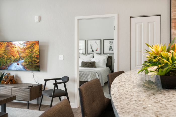 Modern living space with a vibrant wall-mounted TV, cozy bedroom with elegant decor, and a stylish granite countertop adorned with fresh flowers.