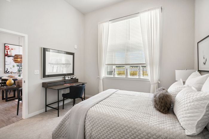 Bright and inviting bedroom featuring a plush bed, large window with natural light, and a cozy workspace setup, perfect for modern urban living.
