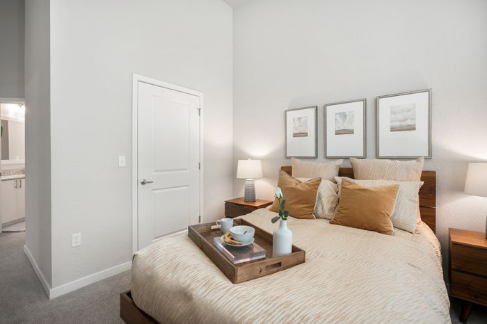 Inviting bedroom with elegant decor, featuring cozy beige bedding, stylish artwork, a chic bedside lamp, and a charming breakfast tray for a relaxing retreat.