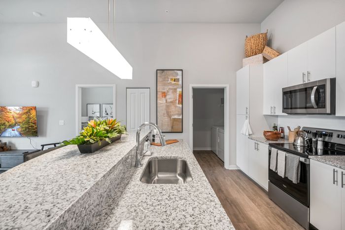 Modern kitchen with sleek granite countertops, stainless steel appliances, and elegant pendant lighting, seamlessly connected to a cozy living area with contemporary decor.