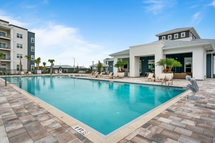 Luxurious apartment complex featuring a pristine outdoor pool with elegant lounge chairs and modern architecture under a clear blue sky.