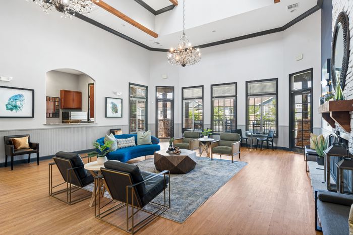 Elegant and spacious living room with high ceilings, modern chandelier, and chic furnishings including a vibrant blue couch and stylish armchairs.