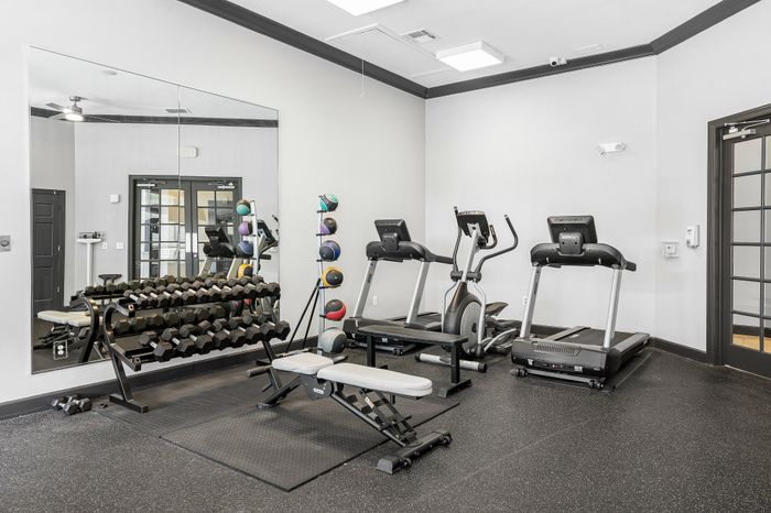Modern apartment gym with state-of-the-art equipment, including treadmills, free weights, and a bench press, perfect for a complete workout.