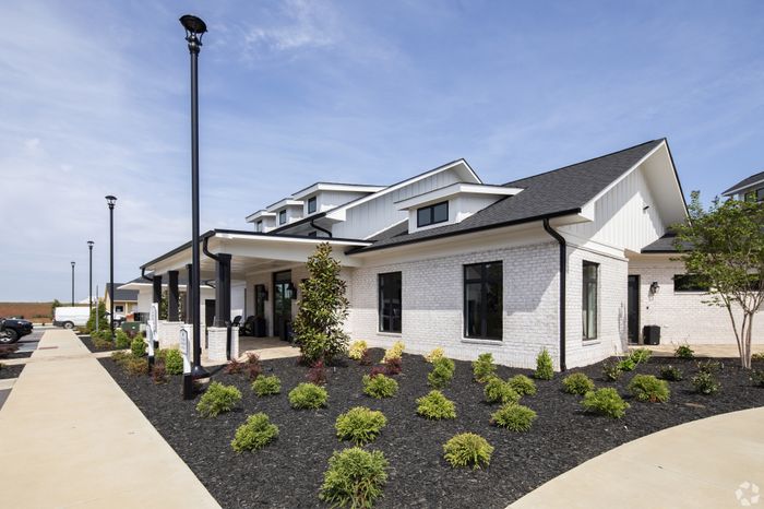 Modern white brick building with elegant black trim, surrounded by landscaped gardens and clear blue skies.