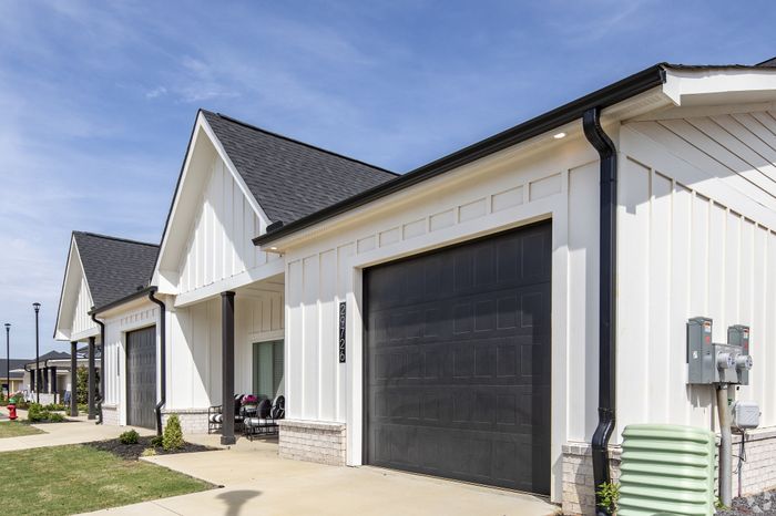 Charming modern farmhouse with stylish black shutters, inviting patio, and manicured landscaping under a bright blue sky.