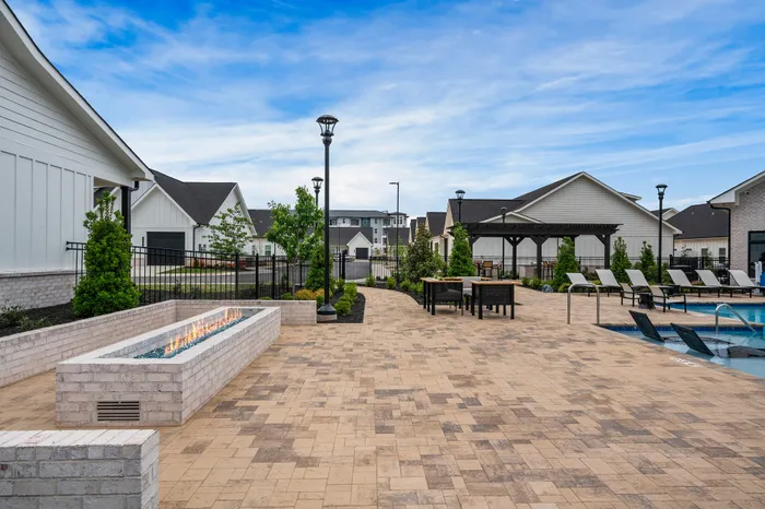Elegant outdoor patio area with modern fire pit, surrounded by lush greenery and comfortable lounge chairs by a sparkling pool.