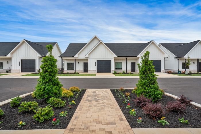 Charming modern cottages with clean white facades and inviting entrances, surrounded by well-manicured greenery and a clear blue sky.