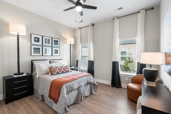 Chic bedroom with modern decor, featuring stylish artwork, elegant floor lamps, cozy bed with textured blankets, and natural light from large windows.