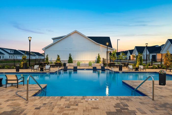 Charming apartment community with a sparkling pool surrounded by stylish seating areas and lush landscaping at sunset.