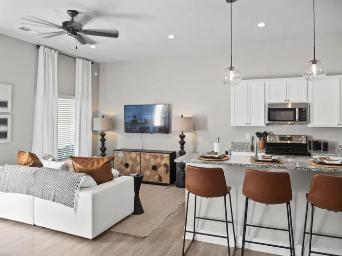 Modern open-concept living area featuring a cozy white sofa, elegant dining bar with chic lighting, and a sleek kitchen with stainless steel appliances.
