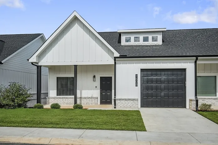 Charming modern home exterior with a gabled roof, sleek black garage, and welcoming front porch, set amidst a lush green lawn.
