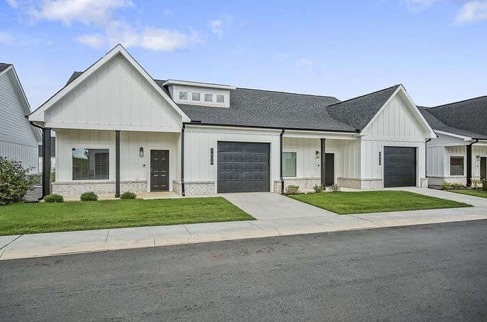 Charming modern duplex with white exterior, sleek garage doors, and manicured lawn, perfect for stylish suburban living.