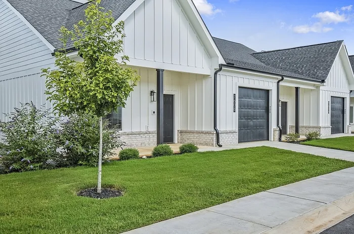 Charming white-beige duplex with sleek black accents, featuring lush green lawns and a welcoming front entrance.
