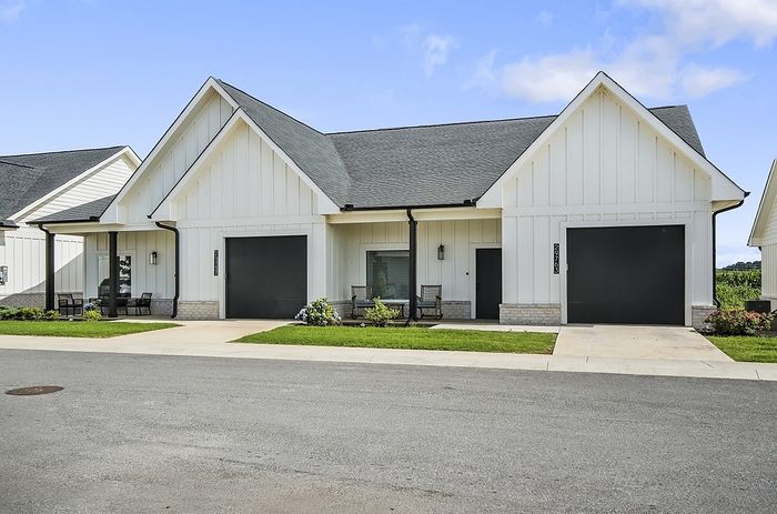 Charming modern home with a sleek black and white exterior, featuring two welcoming front porches and beautiful green lawns.