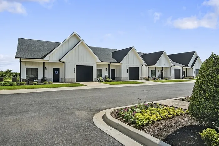 Charming row of modern white townhouses with inviting front lawns and sleek black garage doors, under a bright blue sky.