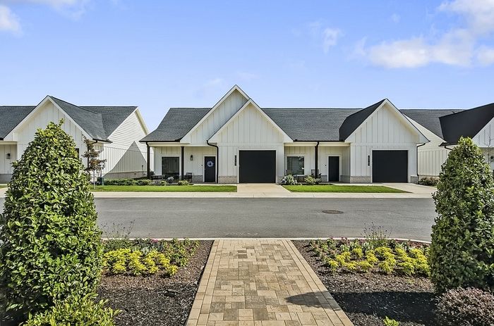 Charming residential street with modern white houses, each featuring sleek black garages, beautifully landscaped front yards, and a welcoming walkway under a clear blue sky.