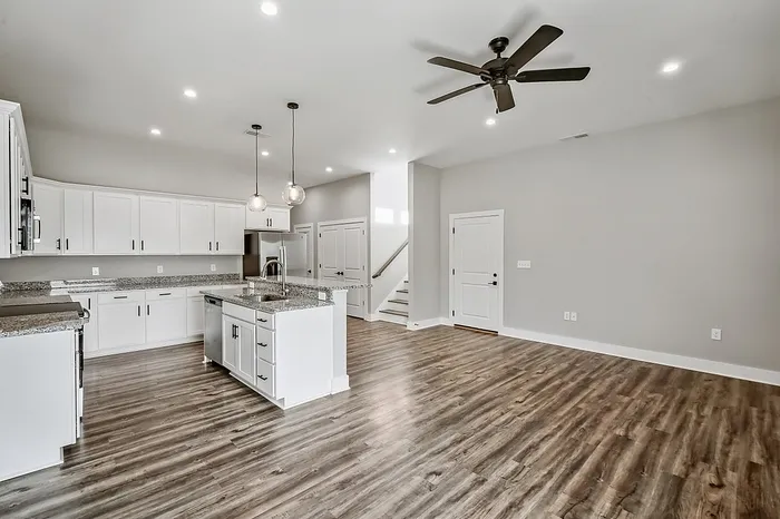 Sleek open-concept kitchen and living area featuring modern white cabinetry, stylish granite countertops, and elegant hardwood flooring.