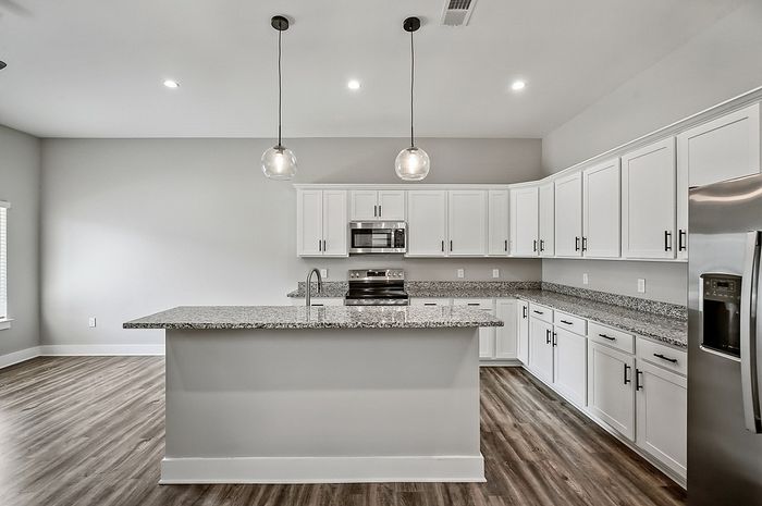 Modern kitchen with sleek white cabinetry, stainless steel appliances, and elegant pendant lighting over a spacious granite island.