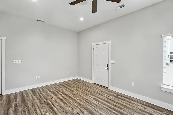 Modern room with elegant wood flooring, bright white walls, and a sleek ceiling fan, creating a spacious and inviting atmosphere.