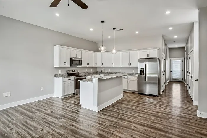 Modern open kitchen with sleek white cabinets, elegant granite countertops, stainless steel appliances, and polished hardwood floors, perfect for entertaining.