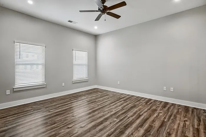 Spacious room with elegant hardwood flooring, modern ceiling fan, and ample natural light from large windows.