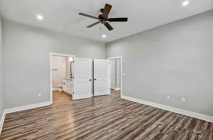 Spacious bedroom with sleek wood flooring, elegant ceiling fan, and access to ensuite bathroom.
