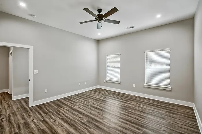 Bright and spacious room with elegant wood flooring, modern ceiling fan, and ample natural light streaming through two windows.