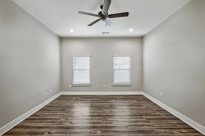 Elegant empty room with polished wood flooring, large windows for natural light, and a modern ceiling fan.