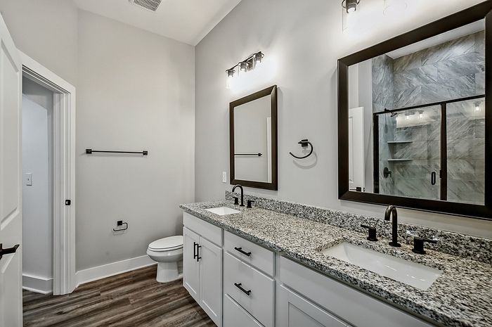 Elegant bathroom featuring dual vanities with granite countertops and sleek modern mirrors, complemented by a luxurious glass-enclosed shower.