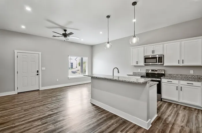Modern open-plan kitchen with sleek granite countertops, elegant pendant lighting, and warm wood flooring.