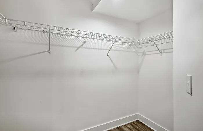 Spacious walk-in closet with sleek white shelving and modern wood flooring, perfect for ample storage.