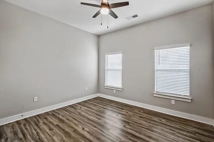 Bright and airy bedroom with sleek hardwood floors, modern ceiling fan, and large windows providing natural light.